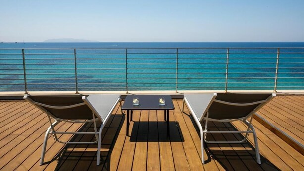 Eine Terrasse mit zwei Liegestühlen und einem Tisch, mit Blick auf das klare, blaue Meer.