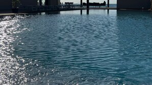 Ein Pool ohne Ende mit freiem Blick auf den Ozean, eine überdachte Lounge und eine moderne Gebäudeanlage.