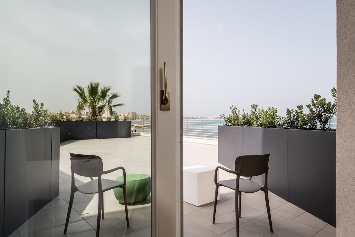 Un balcon avec deux chaises, un pouf vert et une vue sur la mer et le paysage urbain.