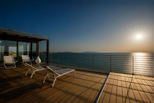Una terraza con sillones de descanso y vista al mar al atardecer.