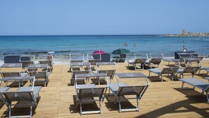 Ein Strand mit Liegestühlen und Sonnenschirmen auf einer Holzterrasse mit Blick auf das Meer.