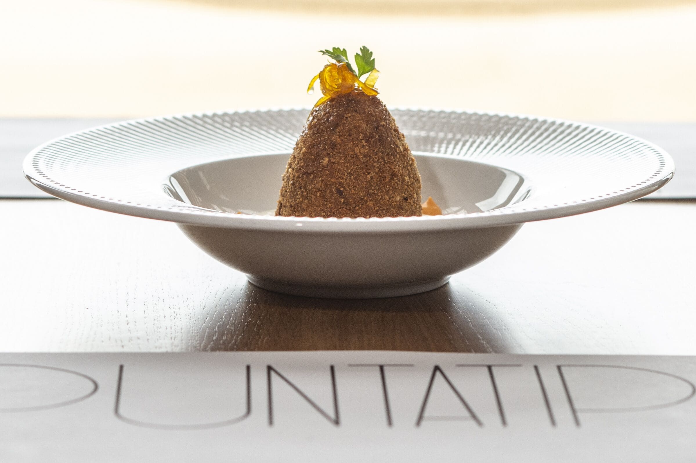 A dessert on a white plate with a textured rim, placed on a table with a menu in front.