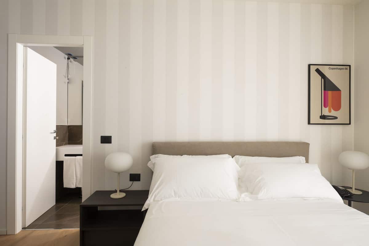 Une chambre d’hôtel avec un lit, des tables de chevet, une petite table, une lampe fixée au mur et un tableau encadré.