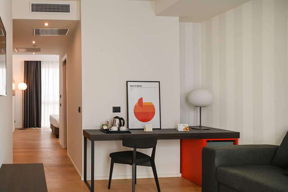 Une chambre d’hôtel moderne équipée d’un bureau, d’une chaise, d’un lit et d’une œuvre d’art encadrée au mur.