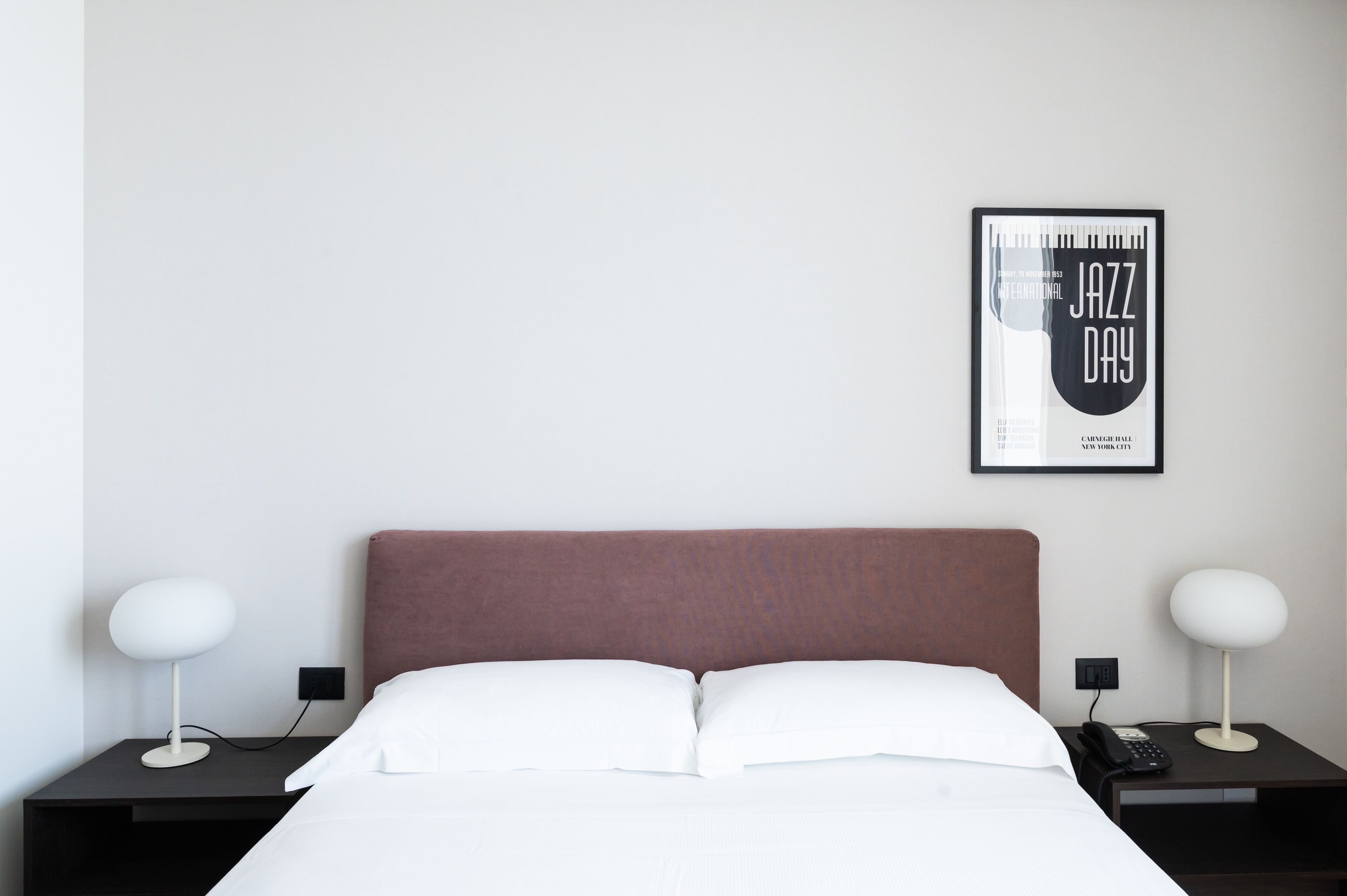 Habitación de hotel con una cama grande, dos mesitas de noche, un cartel enmarcado en la pared y una lámpara moderna en cada mesita.