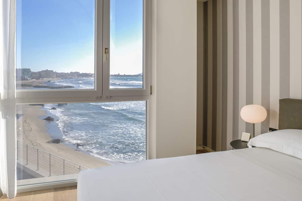 Une chambre avec une grande fenêtre donnant sur une plage et l’océan.