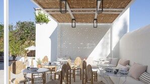 Un patio al aire libre con mobiliario de mimbre, paredes blancas y una pérgola.
