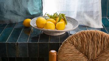 Un cuenco de limones sobre una superficie de azulejos, con una cesta trenzada y una silla de madera.