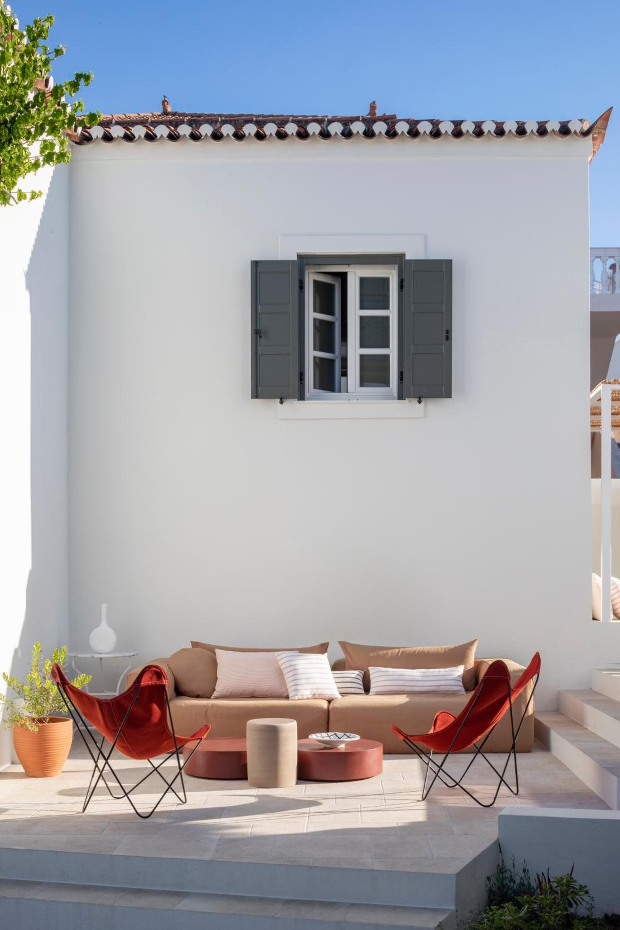 Un espace extérieur moderne aménagé avec un canapé, deux chaises rouges et une petite table.