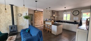 A modern kitchen with a central island, wooden cabinets, and a stove. There is a blue sofa and a wooden table in the living area.