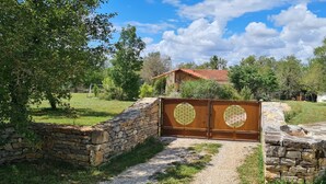 Un muro de piedra con una reja metálica que da a una casa con techo rojo.