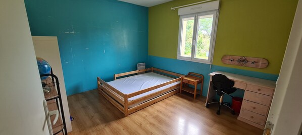 A bedroom with a wooden bed, a desk, a chair, and a window.