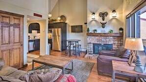 Amplia sala de estar con chimenea, sofá de cuero y una cocina al fondo.