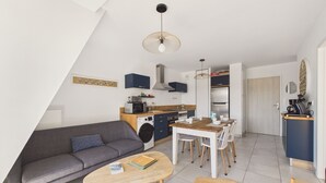 En modern lägenhet med en soffa, ett matbord, stolar, en tvättmaskin och ett litet kök.