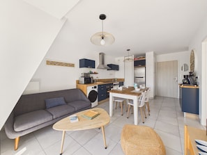 A modern apartment with a sofa, dining table, chairs, a washing machine, and a kitchenette.