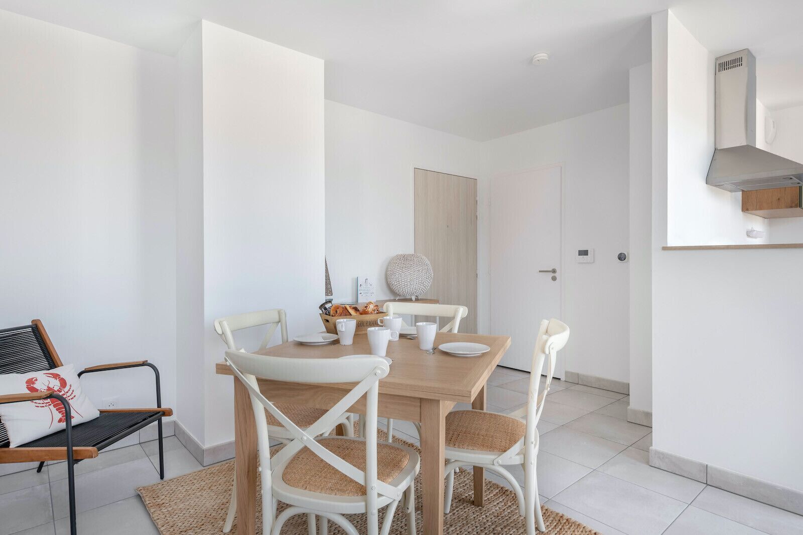 Un espace repas moderne avec une table en bois et des chaises blanches, un panier de pain et un élément décoratif mural.