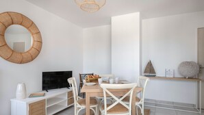 Un comedor moderno con una mesa de madera, sillas blancas, un televisor y una cesta de pan.