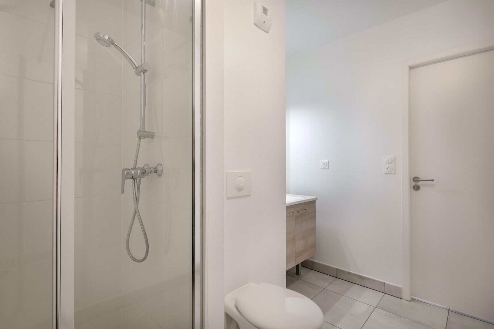 Moderni kylpyhuone, jossa on lasiseinällä varustettu suihku, wc ja pesuallas, jonka alla on puinen allaskaappi.