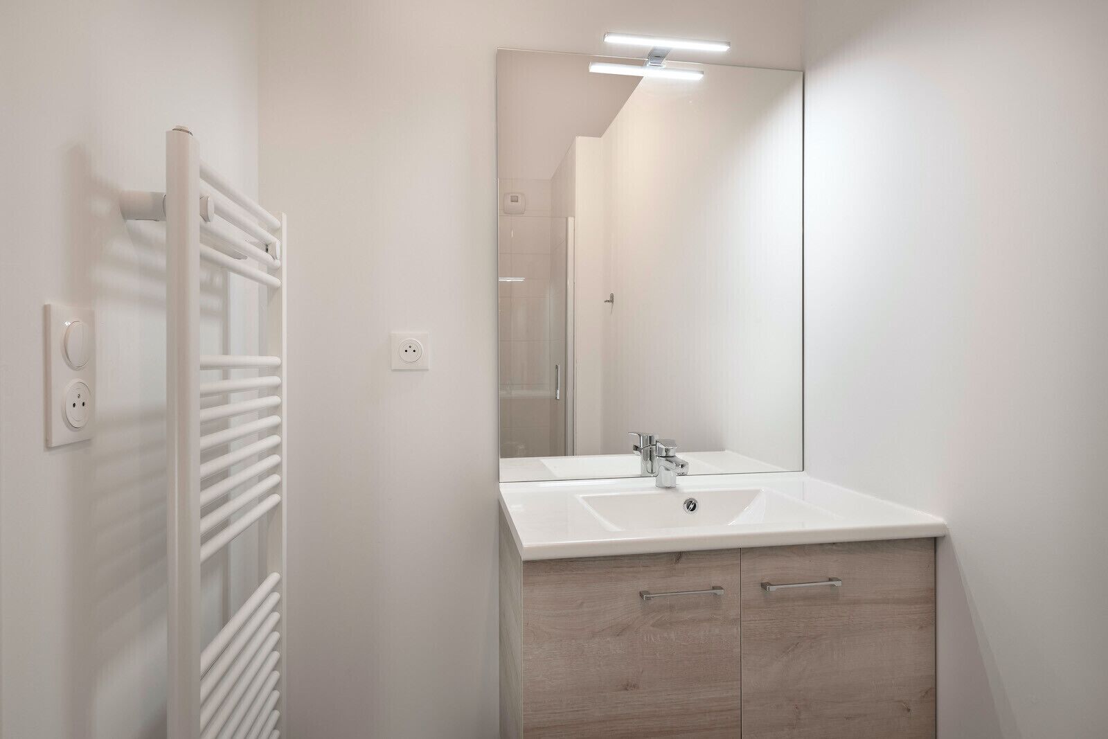 Uma casa de banho moderna com uma pia branca, espelho e porta-toalhas.