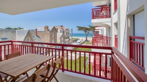 A balcony with a wooden table and chairs, overlooking a beach and buildings. - Nice flat for 6, sea view, 50m from the beach (Pléneuf-Val-Andr é)
