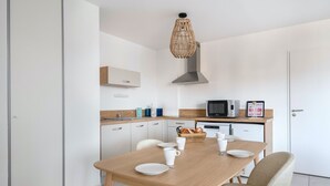 A modern kitchen with white cabinets, a wooden dining table, and a hanging light fixture. - Nice flat for 6, sea view, 50m from the beach (Pléneuf-Val-André)