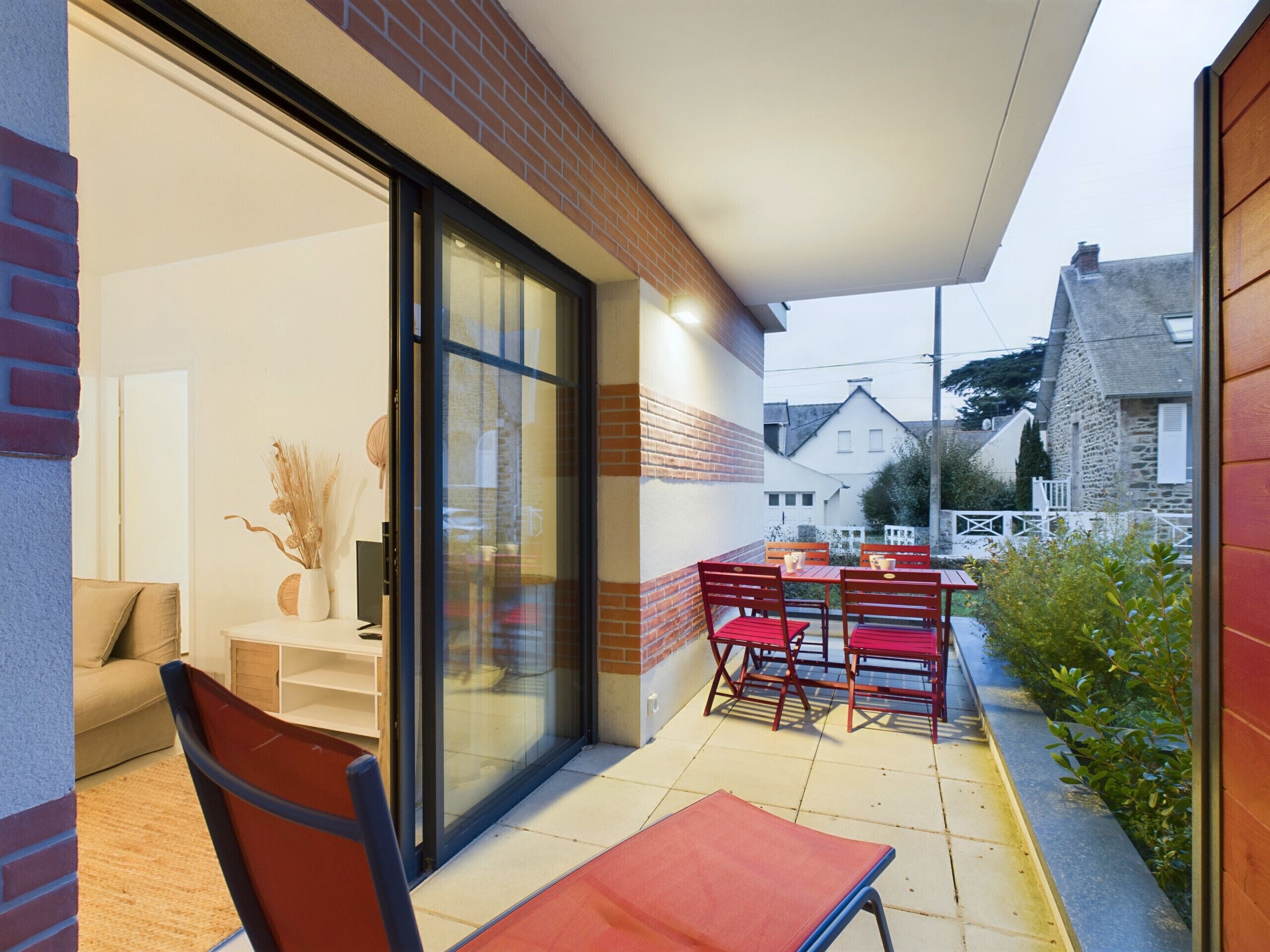 An outdoor patio with a table and chairs, a sofa, and a glass door leading to a room.