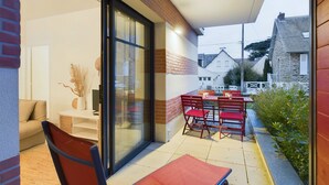 Een terras buiten met een tafel en stoelen, een bank, en een glazen deur die naar een kamer leidt.
