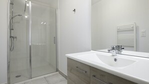 Un baño moderno con ducha de vidrio, lavamanos blanco y espejo.