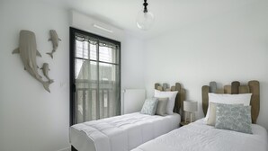 Un dormitorio con dos camas, un ventanal con cortinas translúcidas y una lámpara fijada a la pared.
