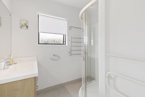 Een moderne badkamer met een douchecabine van glas, een witte wastafel en een raam met gesatineerd glas.