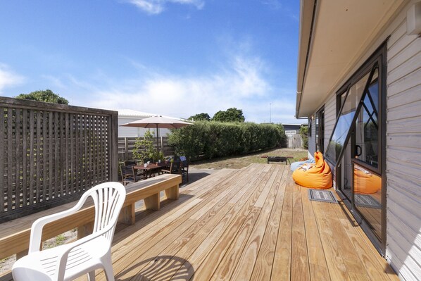 Een houten terras met een tafel en stoelen, een witte plastic stoel en een oranje loungestoel.