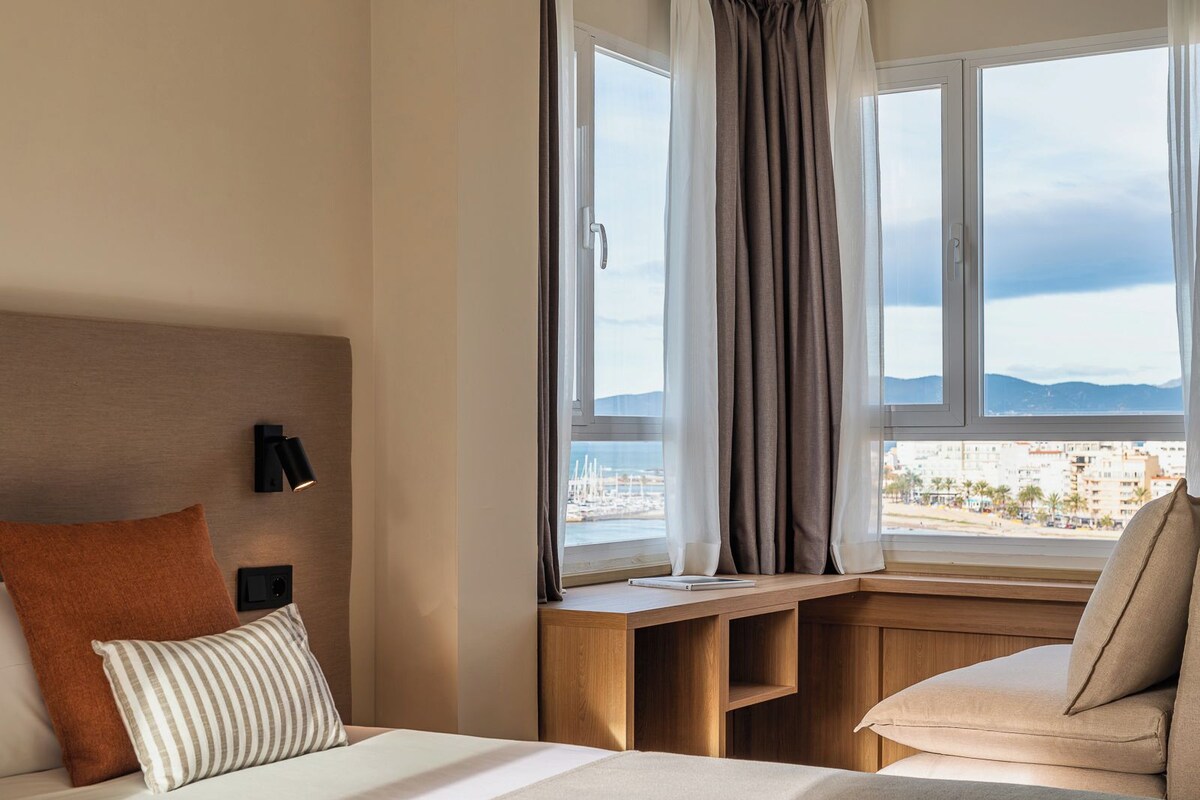 Une chambre d’hôtel avec un lit, un bureau et une vue sur la ville et les montagnes.