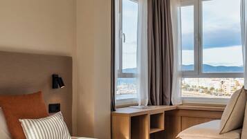 A hotel room with a bed, a desk, and a view of the city and mountains.