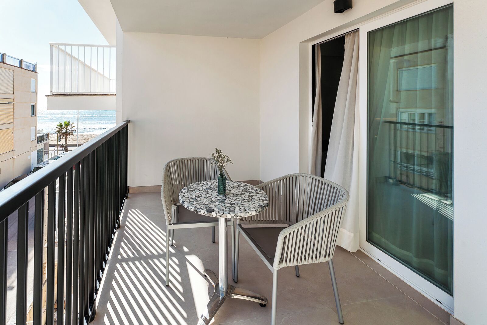 Un balcon avec une table ronde et deux chaises, une vue sur la plage et une porte vitrée.
