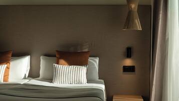 A modern hotel room with a bed, pillows, a bedside table, a wall-mounted light, and a window with curtains.
