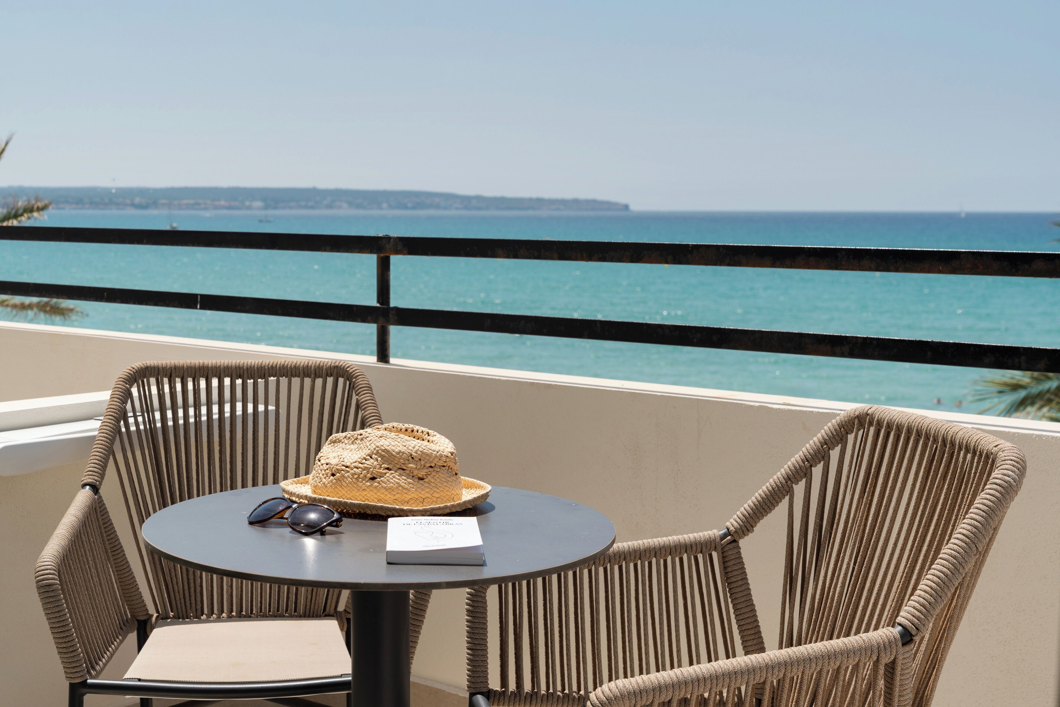 A balcony with wicker chairs, a table, a hat, and sunglasses.