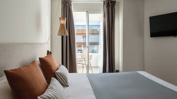 Habitación de hotel con una cama grande, televisor de pantalla plana y balcón con vistas a la ciudad.