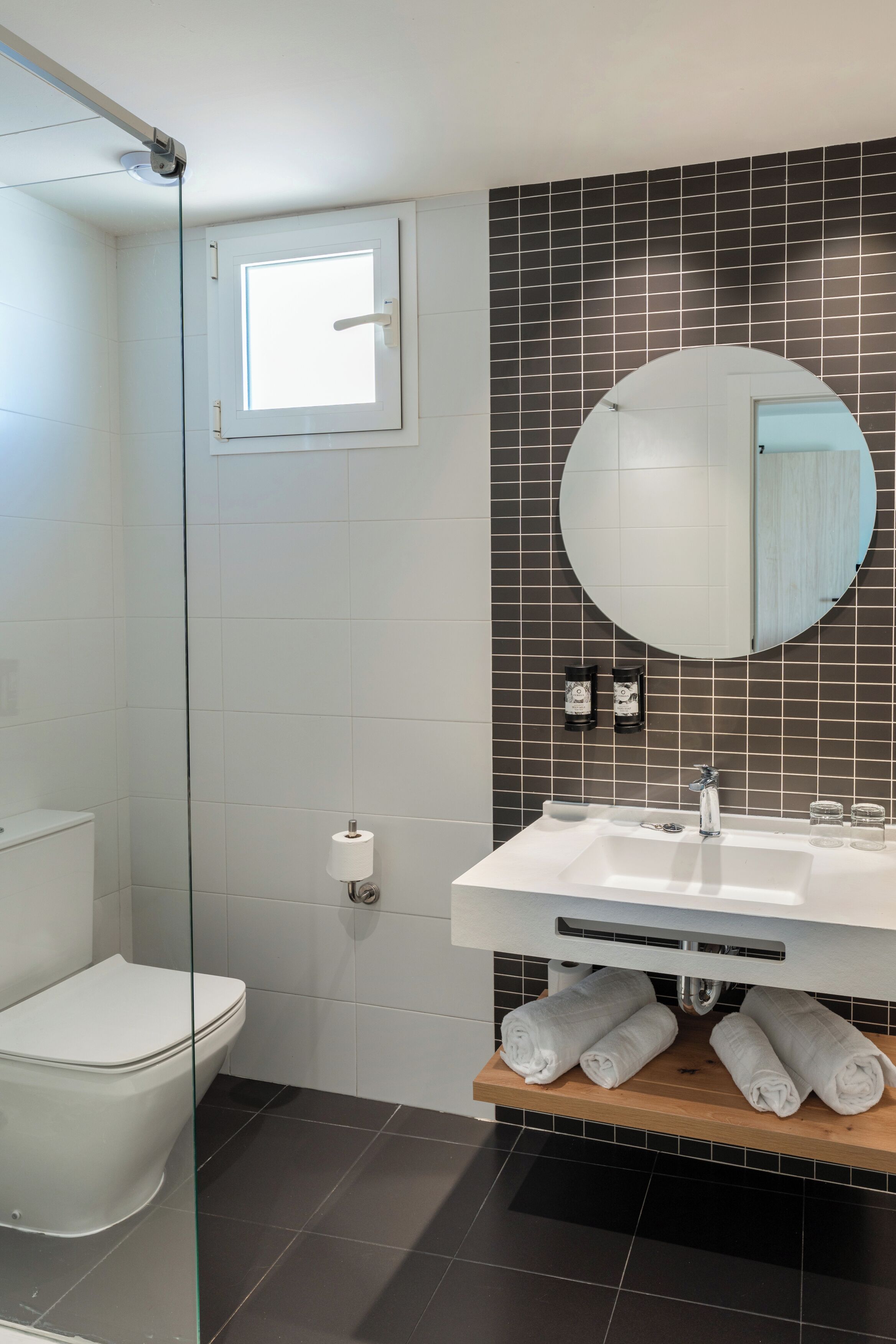 A modern bathroom with a toilet, a glass shower enclosure, a sink with a mirror, and a towel rack.