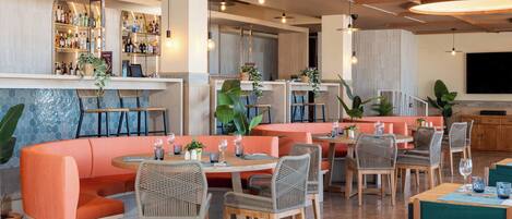 Un restaurante con barra, disposición de mesas y una pantalla de televisión.