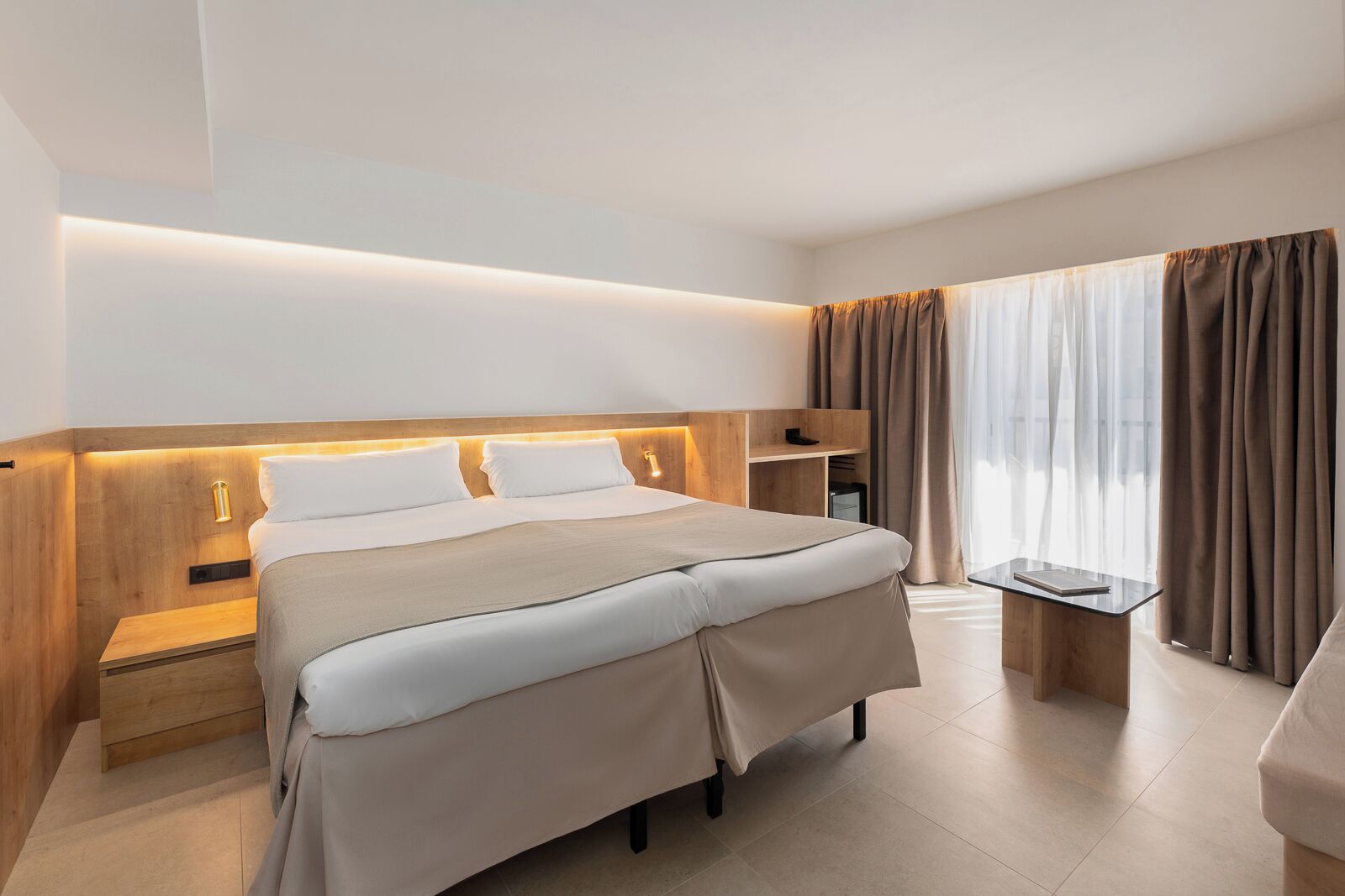 Una habitación de hotel moderna con una cama grande, mesitas de noche, un escritorio y una ventana con cortinas.