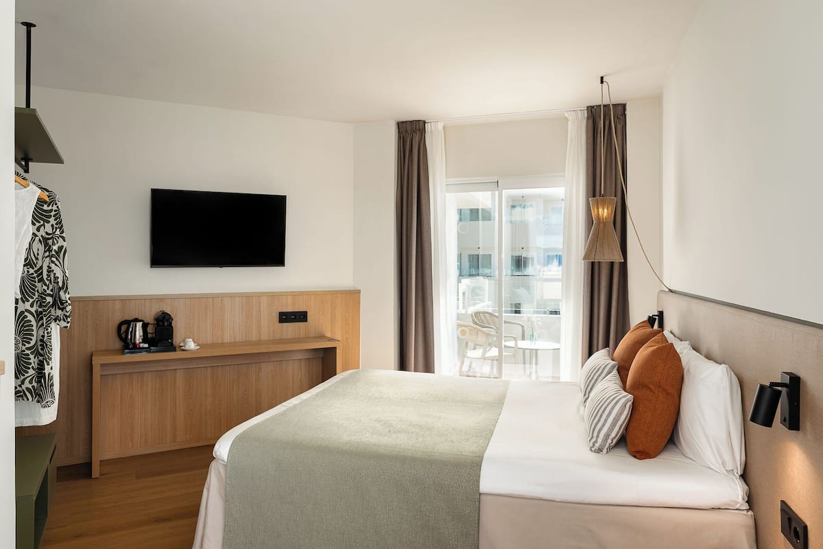 A hotel room with a bed, a TV, a desk with a coffee maker, and a balcony with a view.