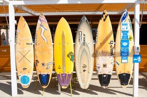 A row of surfboards leaning against a white structure with a wooden roof.
