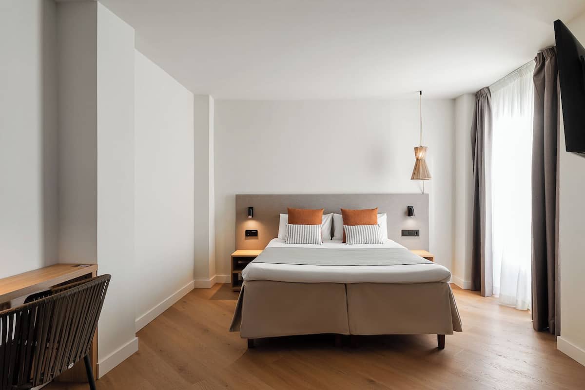 A modern hotel room with a large bed, bedside tables, a desk, and a chair.