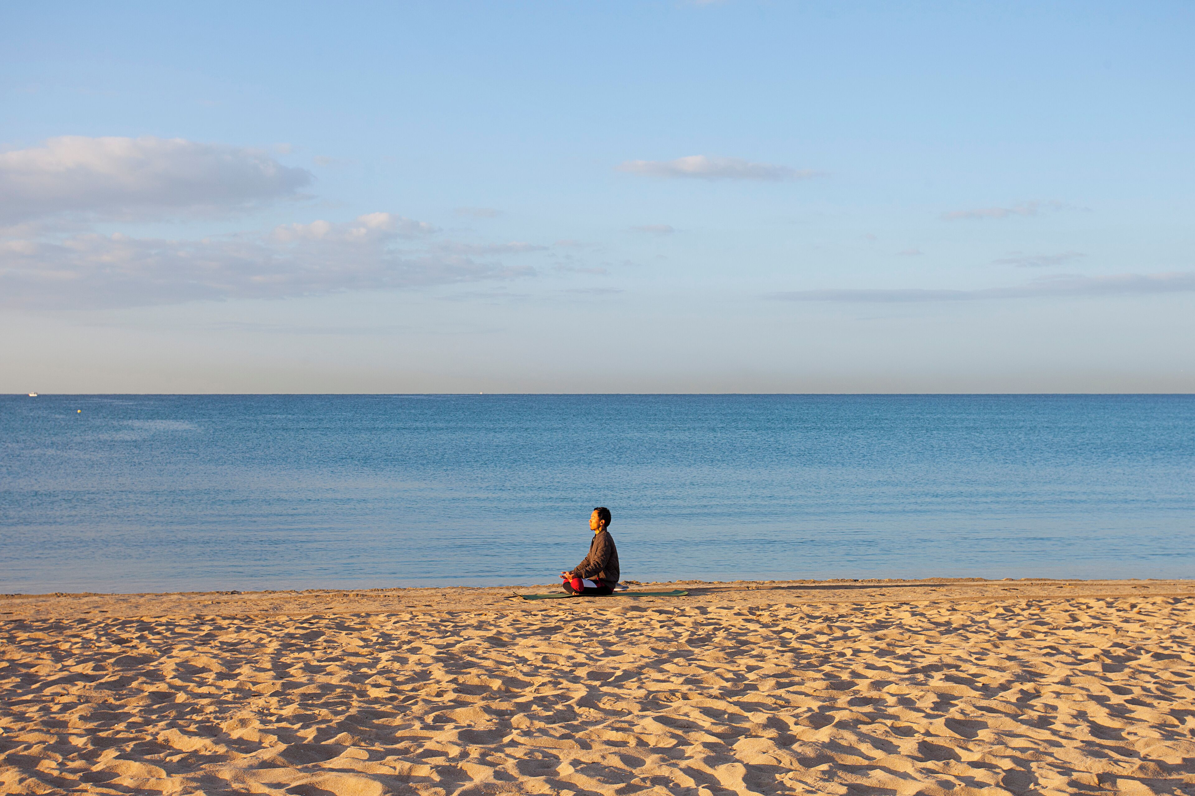A person sitting on a sandy beach facing the ocean.