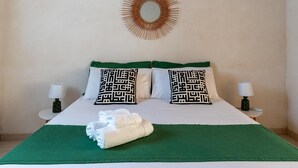 A neatly made bed with green and white bedding, two patterned pillows, a decorative wall mirror, and two bedside lamps. - Villa Vanessa - Noto (Noto)