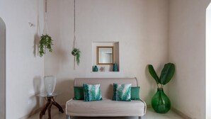 A living room with a sofa, a glass table, a hanging plant, a mirror, and a green vase. - Villa Vanessa - Noto (Noto)