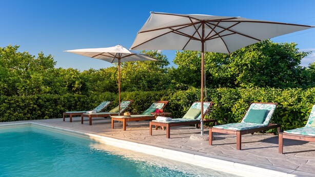 A poolside area with lounge chairs and umbrellas, surrounded by greenery. - Villa Vanessa - Noto (Noto)