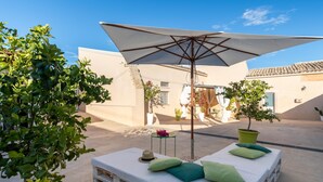 A sunlit outdoor seating area with a white umbrella, wooden benches, and potted plants. - Villa Vanessa - Noto (Noto)