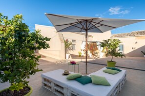 A sunlit outdoor seating area with a white umbrella, wooden benches, and potted plants.