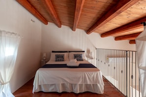 A bedroom with a wooden ceiling, a bed with white bedding and patterned pillows, a nightstand with a lamp, and a balcony with a metal railing. - Villa Linda - Noto - Siracusa (Noto)